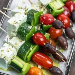 Greek salad kabobs on wooden skewers with a Greek-style vinaigrette drizzled over.
