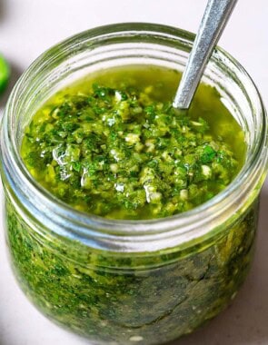 A close up of zhoug in a jar with a spoon.
