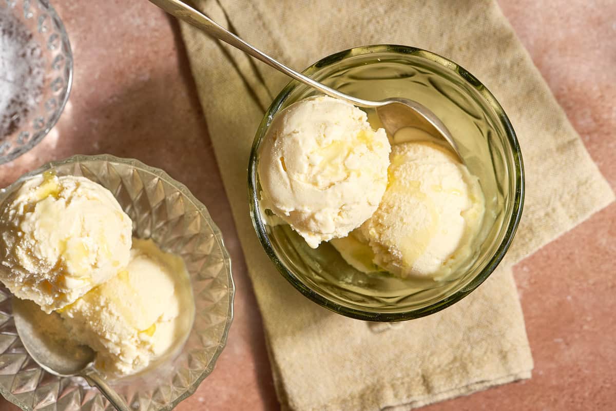 Two bowls of olive oil ice cream with spoons next to a small bowl of flaky sea salt.