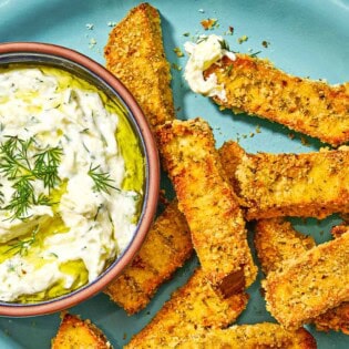 Eggplant fries on a platter with a small bowl of tzatziki sauce.